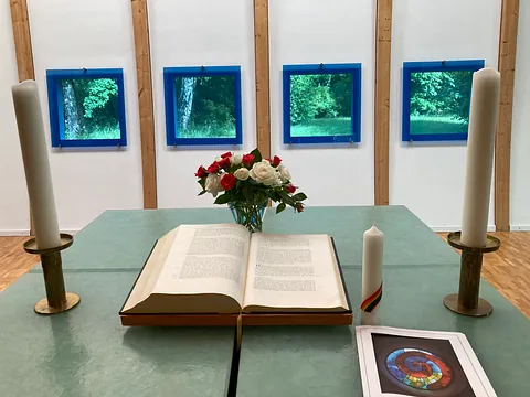 Foto vom Altar mit Kerzen und Blumenstrauß, im Hintergrund die blauen Fenster.