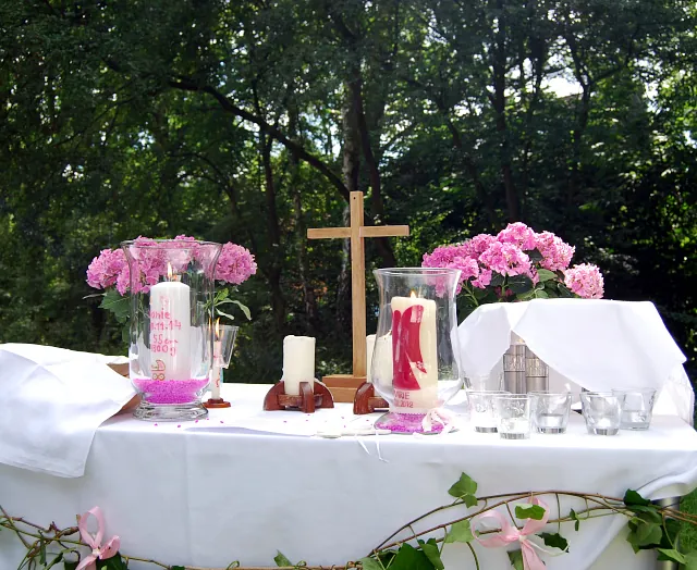 Ein festlich gedeckter Tisch mit Blumen, Kerzen und einem Holzkreuz im Freien