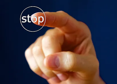  Eine Hand drückt einen runden, weißen Knopf mit der Aufschrift "Stop" vor einem blauen Hintergrund.